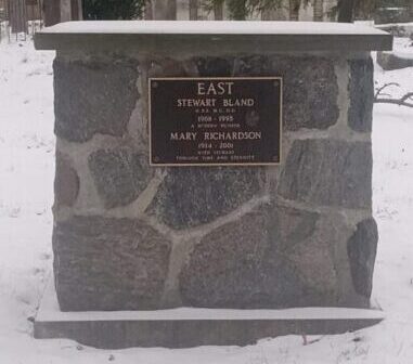 Une pierre tombale carrée faite de roches grises cimentées dans la neige. On peut y lire : « East, Stewart Bland 1908-1995, A modern Pioneer, Mary Richardson, 1914-2001 with Stewart through time and all eternity » (Est, Stewart Bland 1908-1995, un pionnier moderne, Mary Richardson 1914-2001 avec Stewart à travers le temps et pour l'éternité).