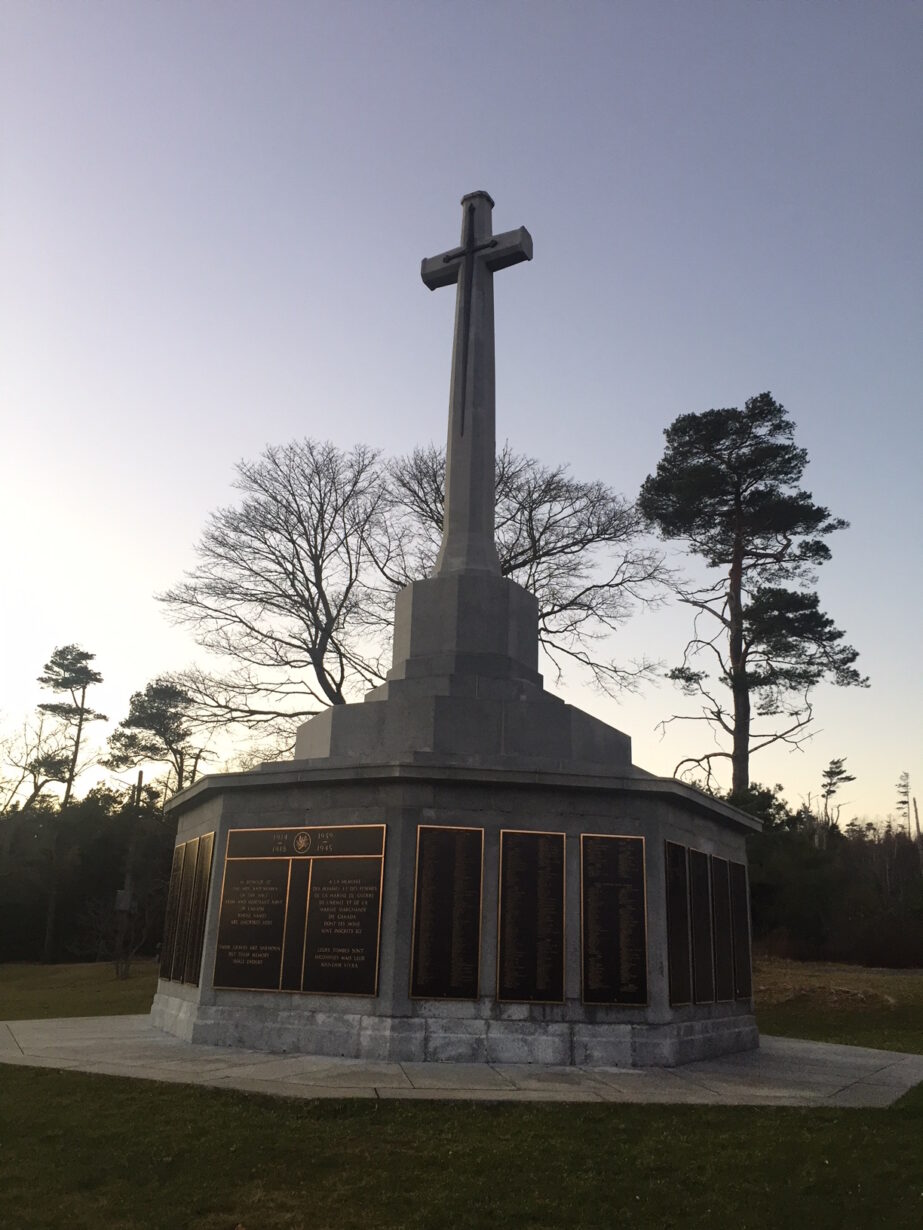 A memorial at dusk. The base is octagonal with plaques on each side. On top is a large stone cross.