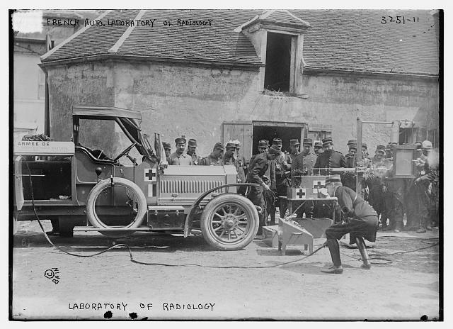 A black and white photo of a military medical truck. Beside it is some medical machinery. There is a wire coming from the truck to the machinery, being held by a soldier. There is a large group of soldiers behind watching. An inscription on the image reads "Laboratory of radiology"