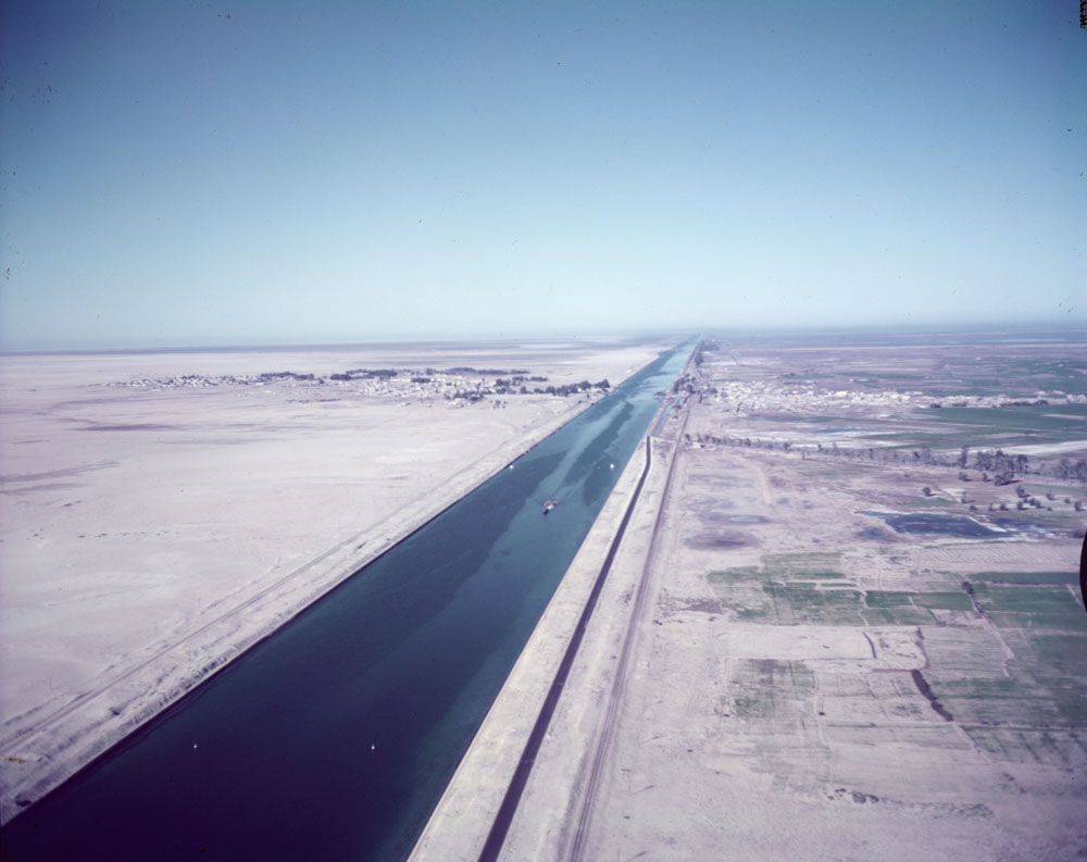 Vue aérienne d'un canal. Le canal traverse un désert avec une ville à proximité.