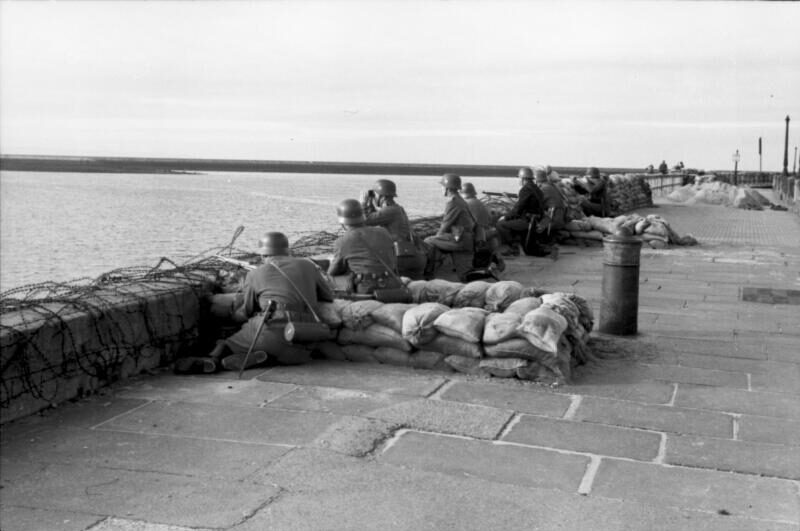 Un groupe de soldats devant un mur barricadé. De l'autre côté du mur se trouve une étendue d'eau.