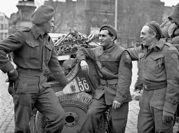 Un groupe de trois soldats discutant devant un véhicule militaire.