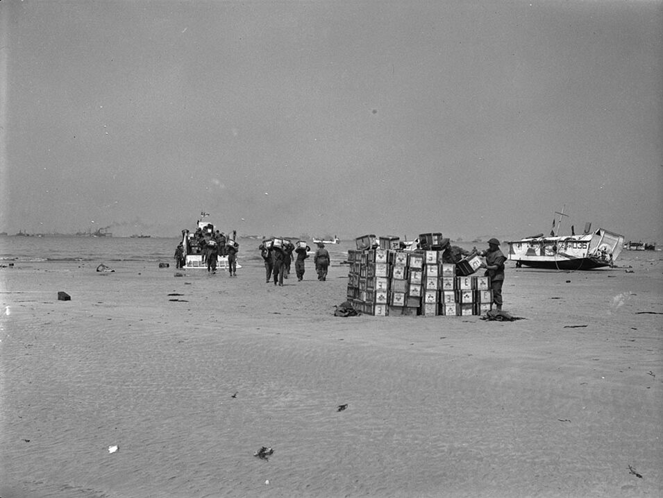 Un groupe de soldats sur une plage. Ils retirent des caisses d'un navire et les empilent sur la plage.