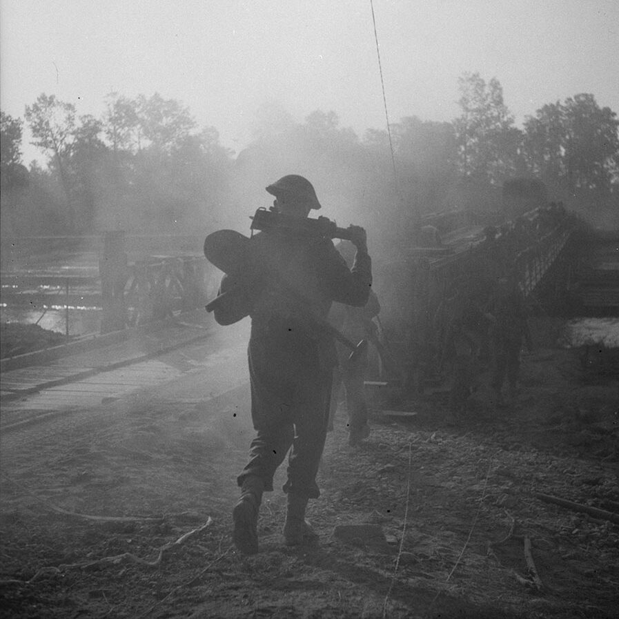 Image d'un soldat s'éloignant de la caméra en direction d'un pont.Il tient du matériel.