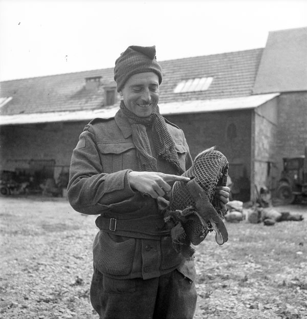 Image en noir et blanc d'un soldat souriant. Il tient un casque. Il y a un trou dans le casque et le soldat le montre du doigt en souriant.