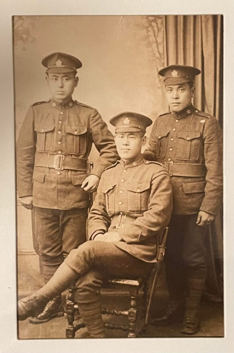 Image sépia de trois Japonais en uniforme. L'homme au centre est assis sur une chaise, tandis que les deux autres sont debout de part et d'autre de l'homme assis.