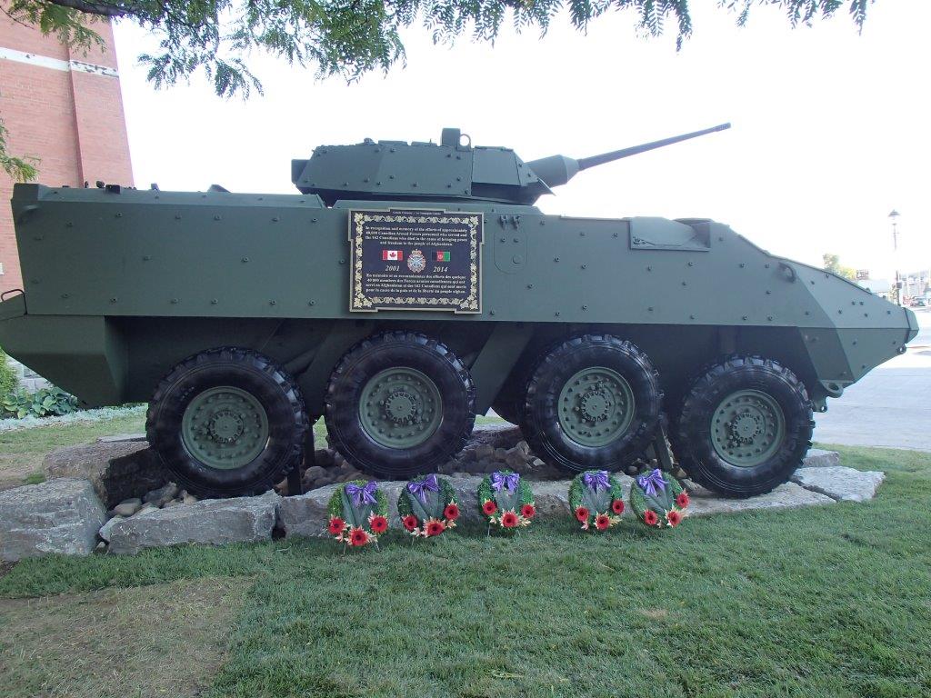 Un véhicule militaire sur un socle de pierres. Sur le côté se trouve une plaque commémorative. Cinq couronnes se trouvent au bas du véhicule, près des rochers.