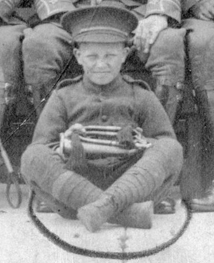 A child in military uniform. he is sitting cross-legged and holding a bugle. 