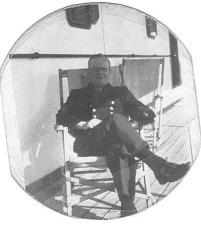 A man wearing a naval uniform sitting in a chair on the deck of a boat.