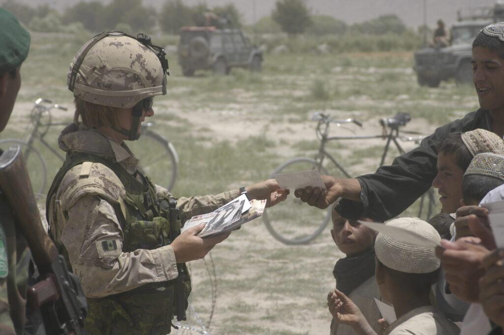 un soldat distribuant des brochures aux Afghans locaux.