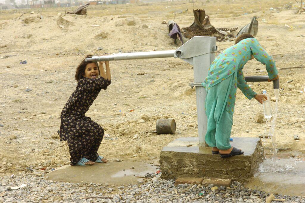 Un enfant joyeux pompe de l'eau à l'aide d'une pompe manuelle. Un autre enfant remplit une bouteille avec l'eau qui s'écoule.