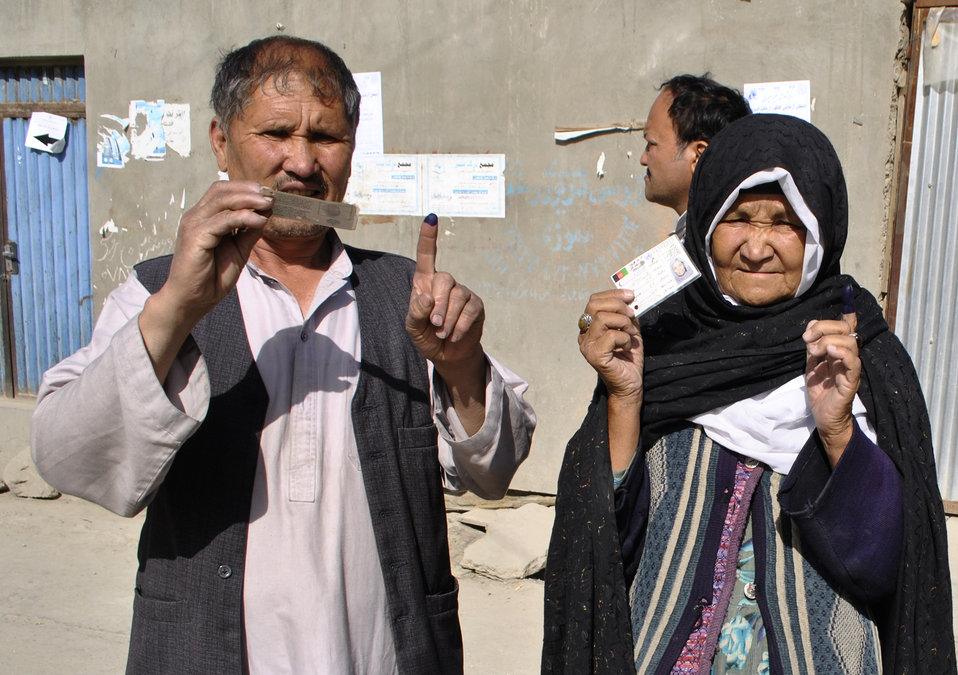 Deux citoyens afghans montrant leur pièce d'identité et leur doigt marqué après avoir voté.