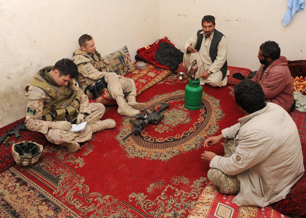 Un groupe de soldats et d'Afghans locaux sont assis sur un tapis et discutent entre eux.