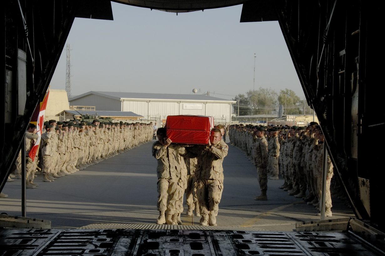 Des soldats canadiens transportent un cercueil recouvert du drapeau canadien à bord d'un avion. D'autres soldats saluent en les regardant.