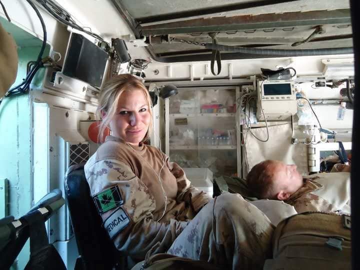 Une femme en uniforme militaire. Elle est assise dans un établissement médical. Un homme est allongé près d'elle.