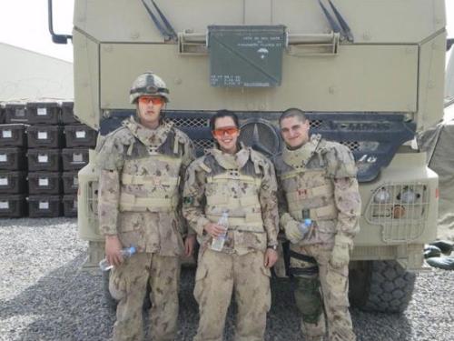 Trois soldats (deux hommes et une femme) debout devant un véhicule militaire.