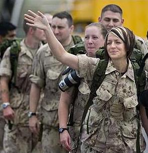 Une rangée de soldats. La femme au premier rang fait signe de la main et sourit.