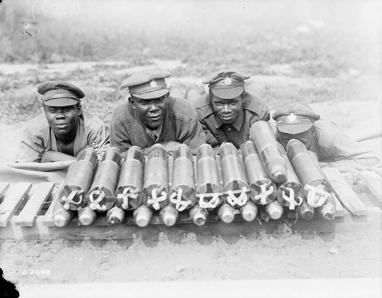 Quatre soldats noirs allongés derrière un tas d'obus militaires.