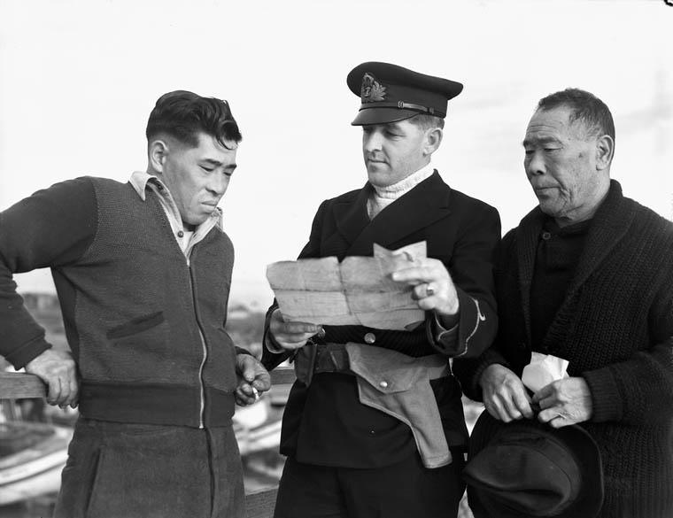 Un homme en uniforme tenant un document. De chaque côté de lui se trouve un homme d'origine japonaise.