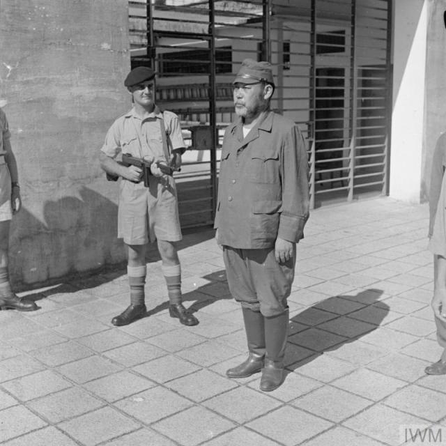 Un soldat japonais se tient immobile. Un autre homme en uniforme pointe une arme dans sa direction.