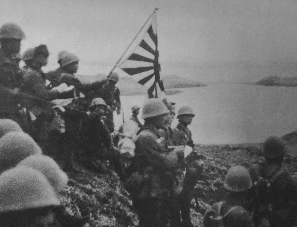 Un groupe de soldats se tient debout sur une île. Ils brandissent le drapeau impérial du Japon.