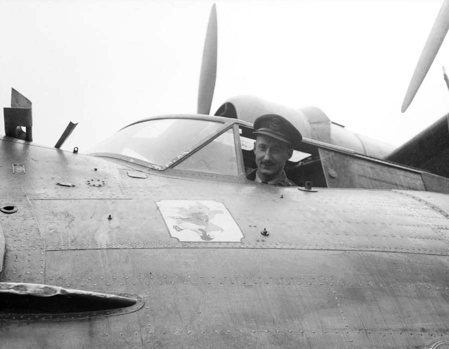 Un homme en uniforme assis dans un avion. Il sourit.