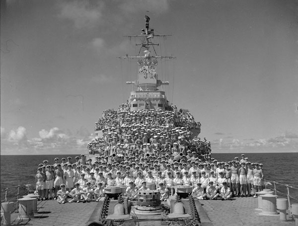 Un grand groupe d'hommes debout devant un bateau, posant pour une photo.