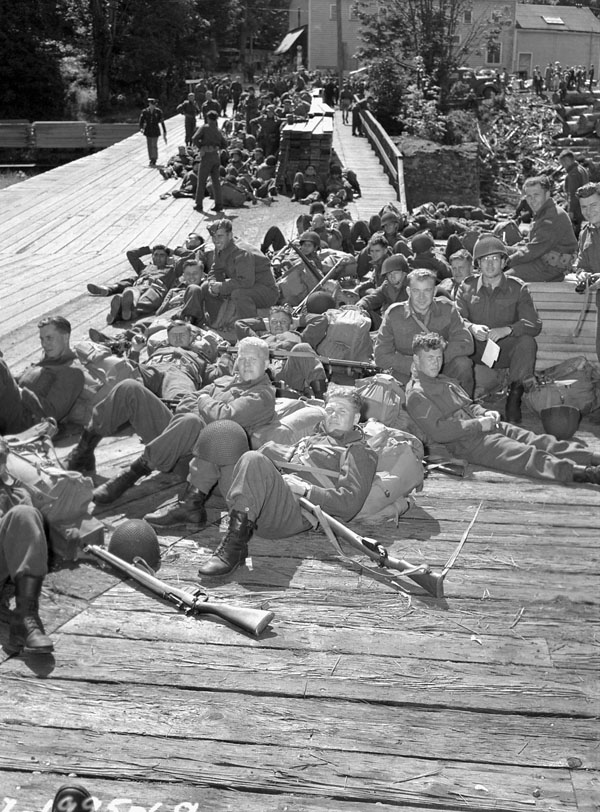 Un groupe de soldats sur un quai. Certains sont assis, d'autres allongés.