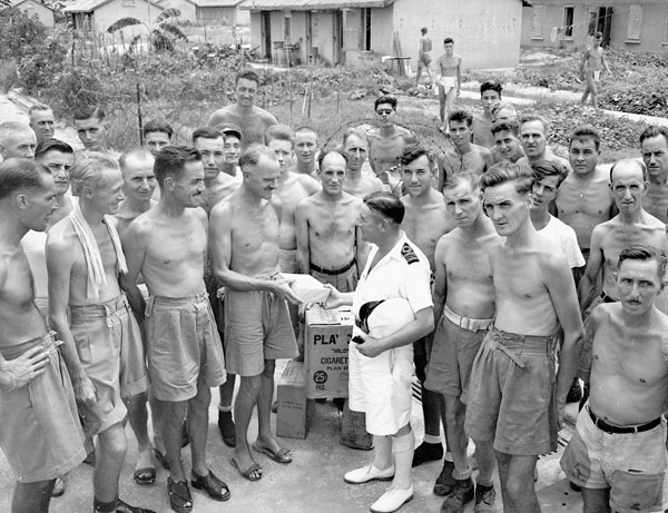 Un groupe d'hommes en short se fait prendre en photo. L'un d'eux reçoit un colis des mains d'un homme en uniforme.