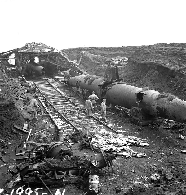 Un groupe de soldats examine les vestiges d'un campement japonais. Parmi ces vestiges, on trouve des sous-marins détruits, une voie ferrée et du matériel en ruine.