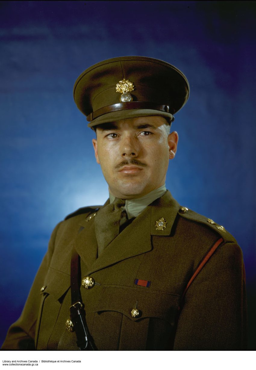 Portrait d'un homme en uniforme. Il regarde légèrement sur le côté et porte une moustache fine.