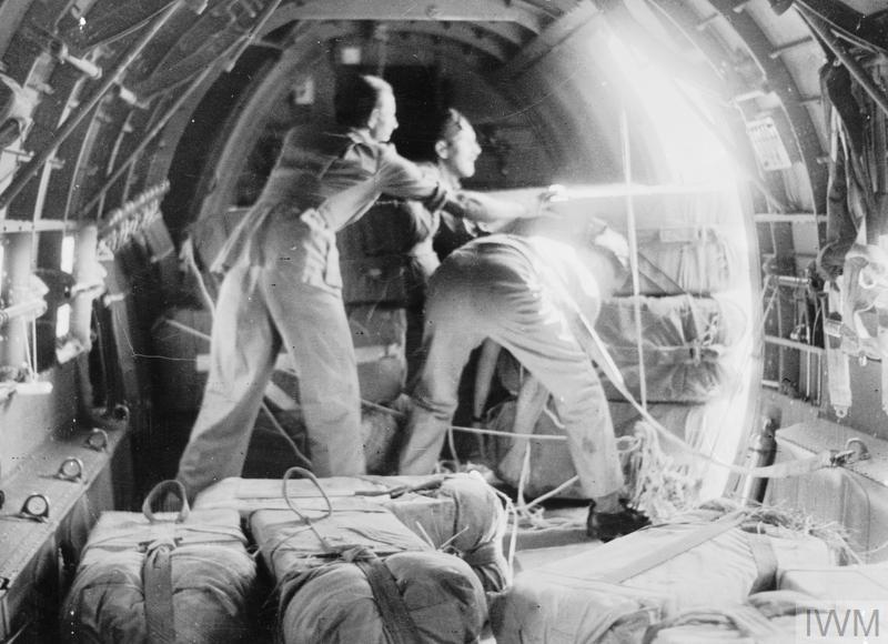 un groupe d'hommes en train de pousser de gros colis hors de la porte ouverte d'un avion.