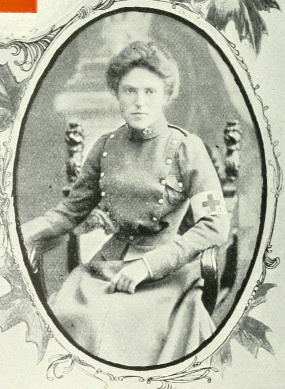 A seated woman in a nursing uniform. She has an armband with a cross on it.